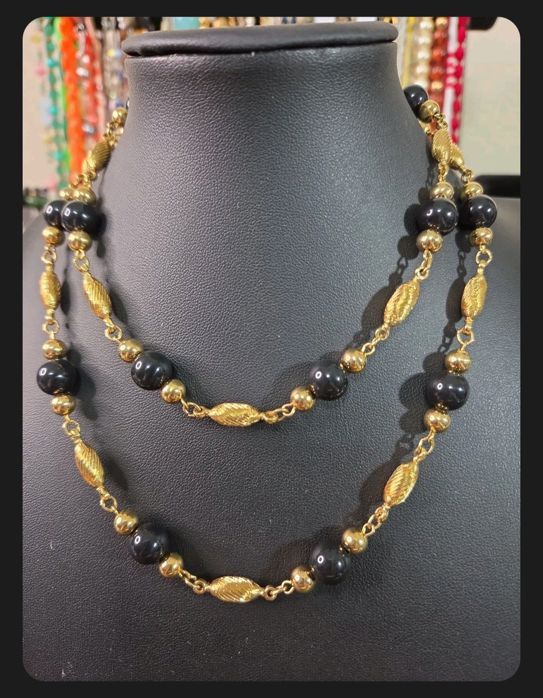 Oddly Darling Vintage long necklace with polished black beads and textured gold-tone metal spacers on a display bust.