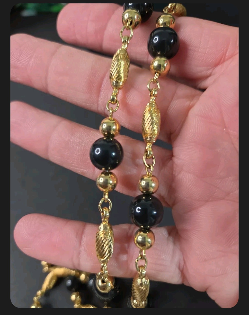 Oddly Darling Vintage long necklace with polished black beads and textured gold-tone metal spacers held in a hand.