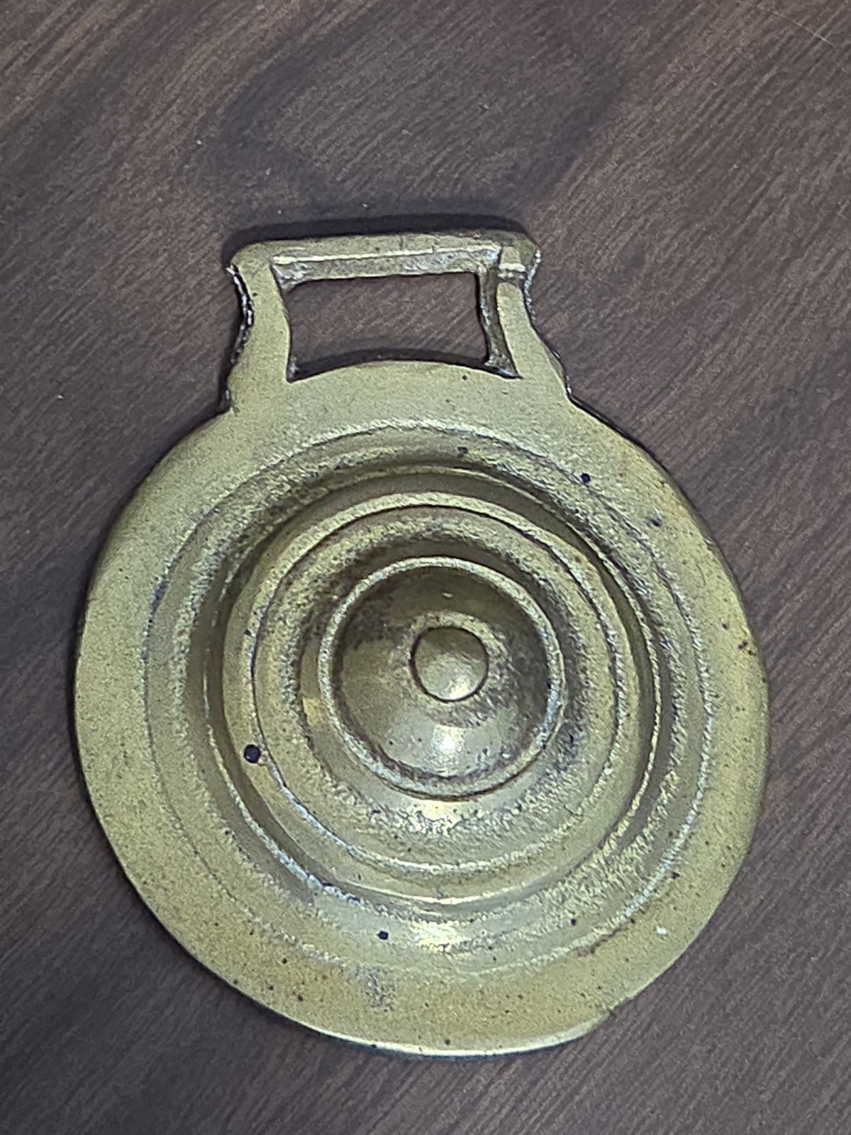 Oddly Darling Vintage brass horse harness medallion with a circular design and warm patina on a dark wooden surface.