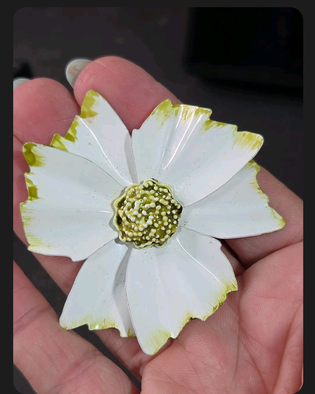 Oddly Darling Vintage enamel flower brooch with white petals, green tips, and a textured beaded center held in a hand.