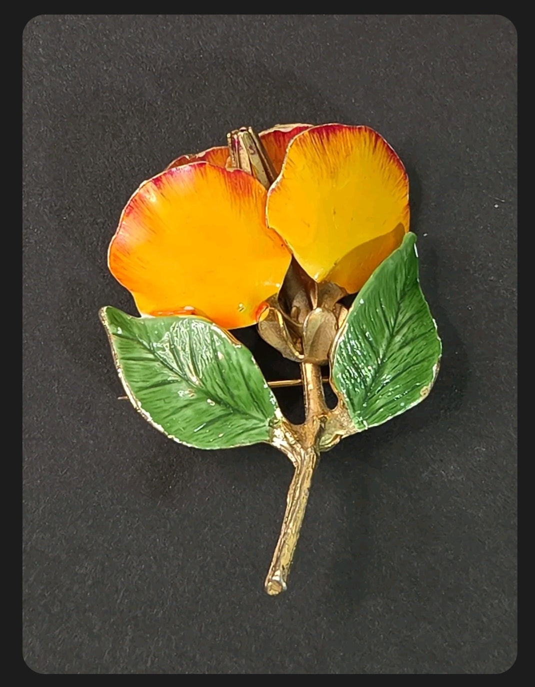 Oddly Darling Vintage floral brooch with yellow and orange enamel petals and green leaves on a gold-tone metal stem.