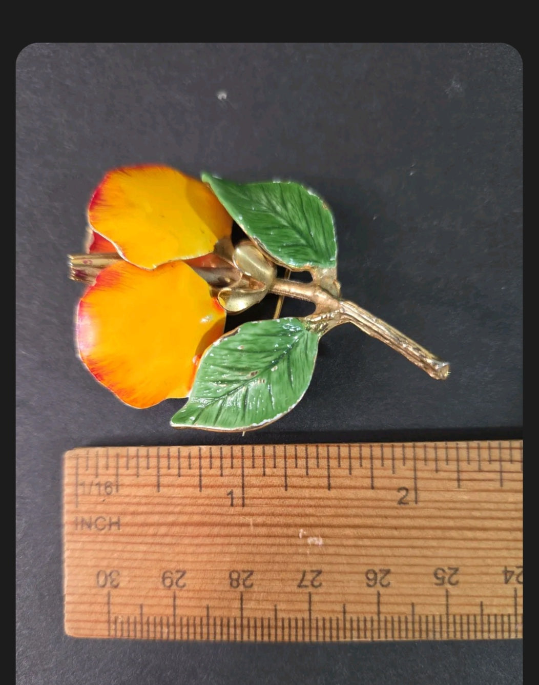 Oddly Darling Vintage floral brooch with yellow and orange enamel petals and green leaves on a gold-tone metal stem.