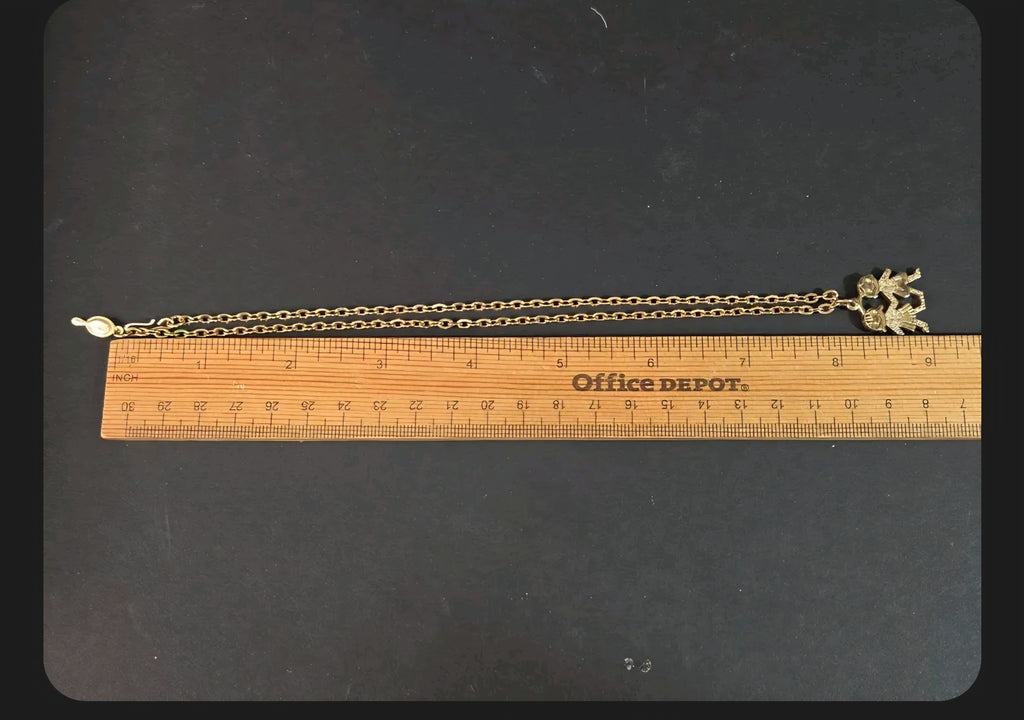 Oddly Darling Vintage gold-tone children charm pendant necklace measured against a wooden ruler on a black surface.