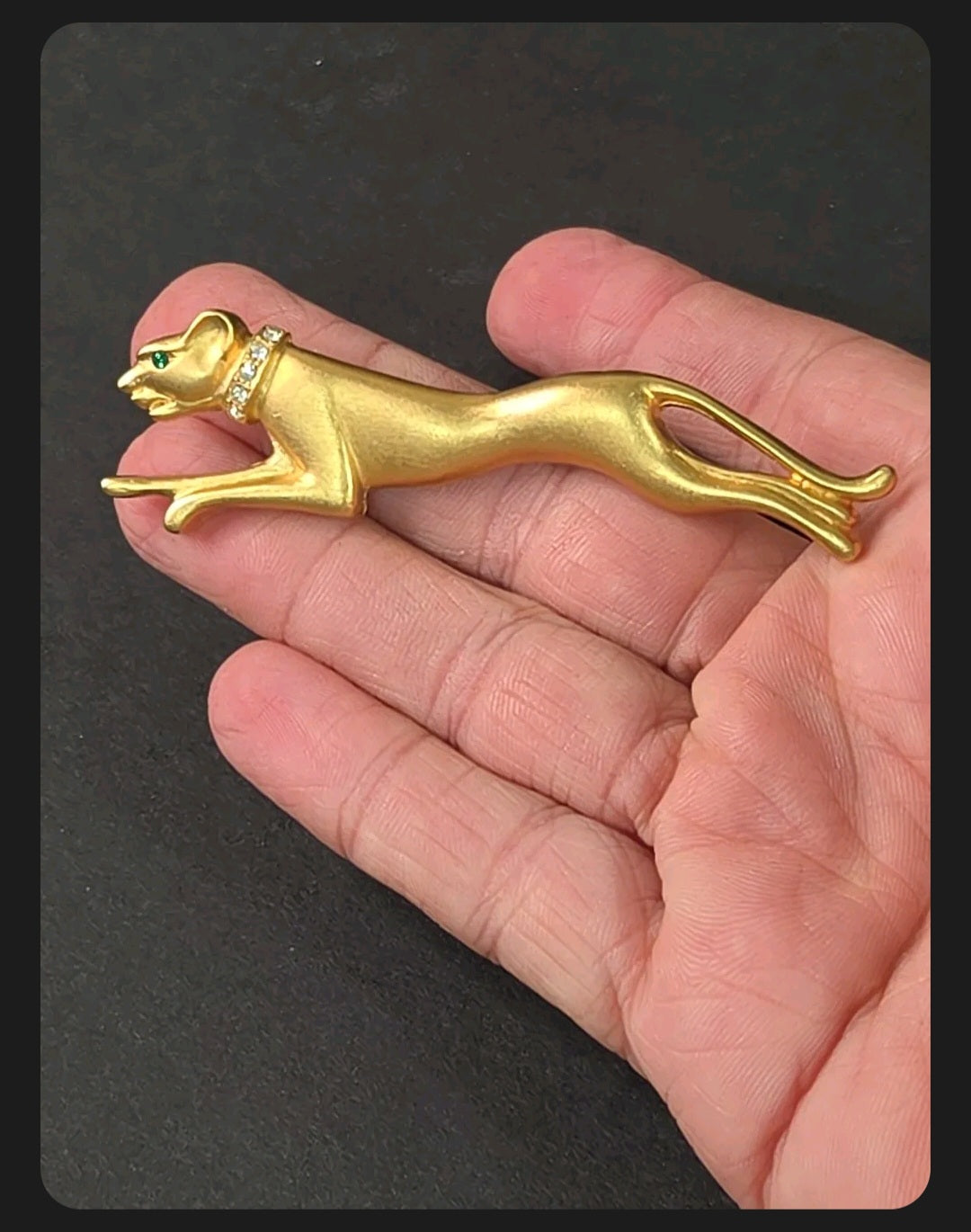 Oddly Darling Vintage brushed gold-tone panther brooch with crystal collar and green stone eye held in a hand.