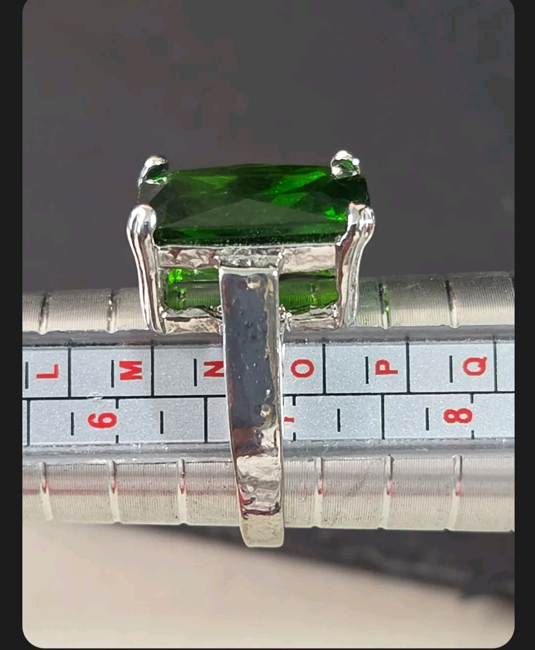 Oddly Darling Vintage emerald-cut green gemstone cocktail ring on a silver metal ring sizer tool