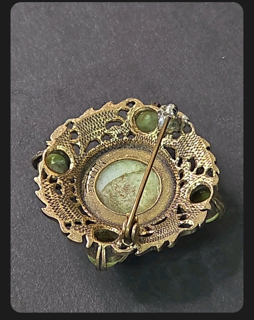 Back view of an Oddly Darling Vintage Miracle brooch showing the signature hallmark and antique-gold metal pin detail.