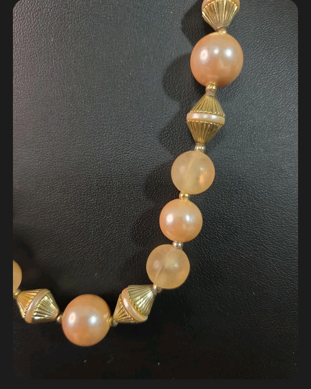 Oddly Darling Vintage necklace with peach faux pearls, frosted beads, and gold-tone fluted spacers on black display.